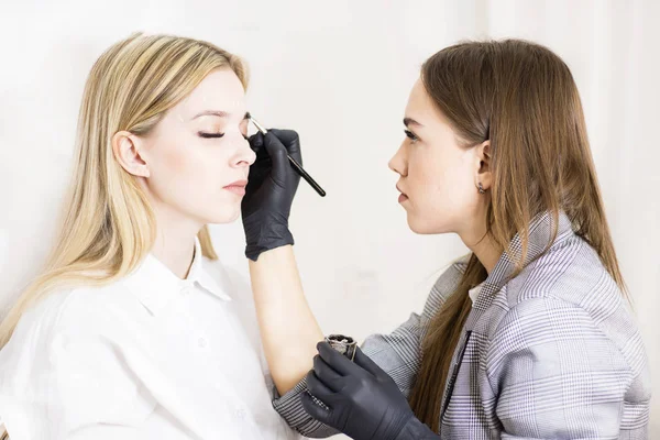 Kadın kozmetolojist güzellik salonunda güzel modellerde kaş düzeltme gerçekleştirir. Kızın yüzü sarışın. Close. Yüz bakımı