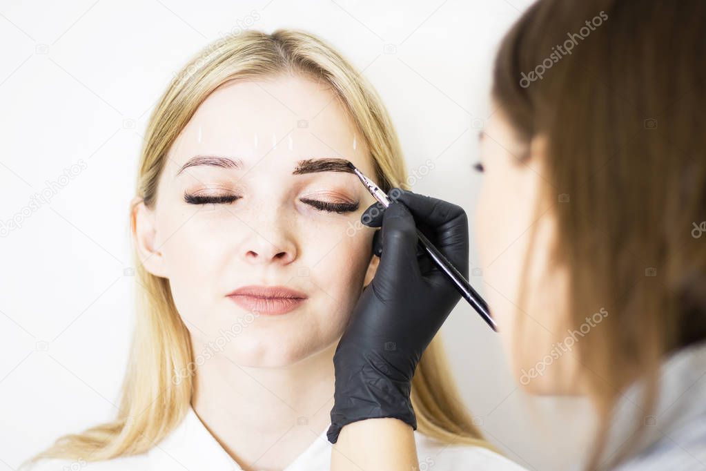 Female cosmetologist performs eyebrow correction on beautiful models in the beauty parlor. The girl's face is a blonde. Close-up. Facial care