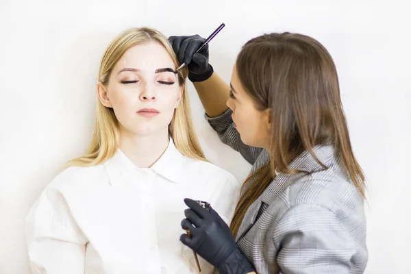 Güzellik uzmanı bir güzellik salonunda güzel bir model kaş düzeltme gerçekleştirir. Kız sarışın. Yüz bakımı. Kına boyama