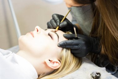 Güzellik uzmanı bir güzellik salonunda güzel bir model kaş düzeltme gerçekleştirir. Kız sarışın. Yüz bakımı. Kına boyama