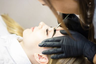 Güzellik uzmanı bir güzellik salonunda güzel bir model kaş düzeltme gerçekleştirir. Kız sarışın. Yüz bakımı. Kına boyama