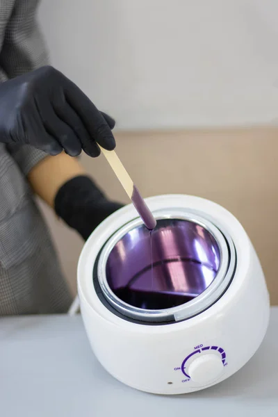 Eyebrow waxing. Hot wax of lilac color of a liquid consistence. Wax heater