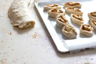 Pişirme tepside yatıyor. Çörek pişirme işlemi. Masada un, hamur, demirbaşlar var.