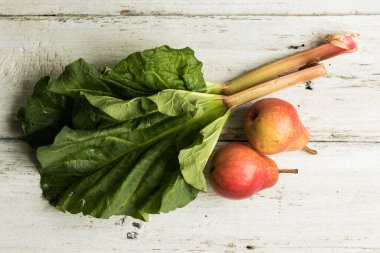 Rubarb sapları ve beyaz ahşap bir arka planda iki armut. Tamamlayıcı renkler. Çimen ve meyve. Yatay yönelim