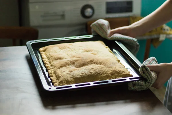 女孩从烤箱里拿出一块蛋糕.用铁钉夹住烤盘.厨房是青绿色的.家庭烹饪 — 图库照片