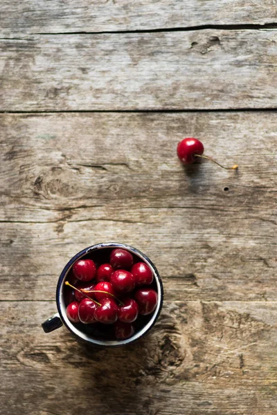 Ripe fresh sweet cherry lies in an old metal mug on a wooden table. Sweet wholesome dessert. Environmental design and minimalism. Copy space and top view — Stock Photo, Image