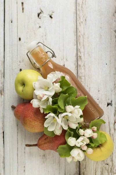 Bottle of apple and pear juice, fresh pears, apples and flowers on a white wooden background. Country style