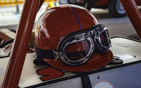 Vintage racing helmet and glasses resting on an antique sports car.