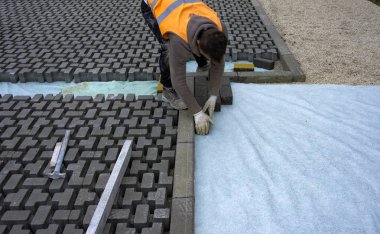 Construction worker laying interlocking paving concrete onto sheet nonwoven bedding sand and fitting them into place. clipart