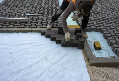 İnşaat işçisi birbirine kenetlenmiş betonu örülmemiş kumun üzerine seriyor ve yerine oturtuyor..