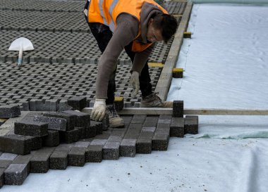 İnşaat işçisi birbirine kenetlenmiş betonu örülmemiş kumun üzerine seriyor ve yerine oturtuyor..