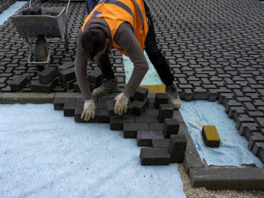 İnşaat işçisi birbirine kenetlenmiş betonu örülmemiş kumun üzerine seriyor ve yerine oturtuyor..