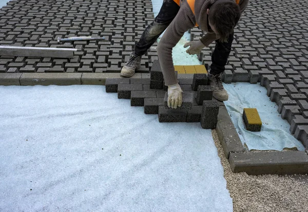 İnşaat işçisi birbirine kenetlenmiş betonu örülmemiş kumun üzerine seriyor ve yerine oturtuyor..