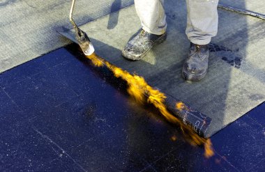 Bitumen çatı keçesinin bir kısmını ısıtıcı meşale ateşiyle eritmek için hazırlayan işçiler