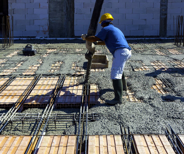 Construction worker compacting liquid cement in reinforcement form work during concreting floors pouring works