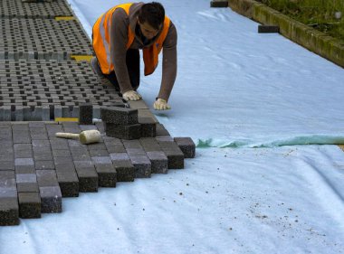 İnşaat işçisi birbirine kenetlenmiş betonu örülmemiş kumun üzerine seriyor ve yerine oturtuyor..