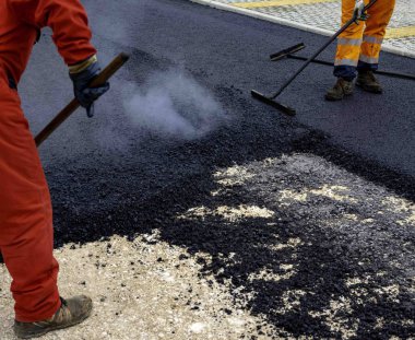 Worker distributes on the edge the asphalt laid out for the construction of a road clipart