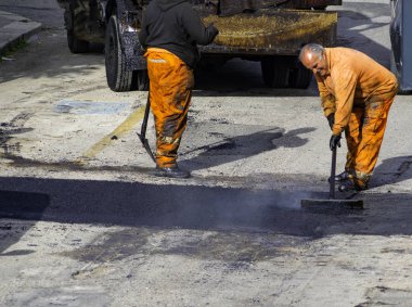 İşçi yoldaki bir tümseği onarmak için yeni asfalt döşemeyi düzenler.