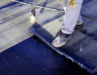 Bitumen çatı keçesinin bir kısmını ısıtıcı meşale ateşiyle eritmek için hazırlayan işçiler