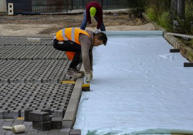 Paving taş işçisi bir şehir caddesinin inşaatı sırasında kaldırımları örülmemiş kumun üzerine yerleştiriyor ve yerine yerleştiriyor..
