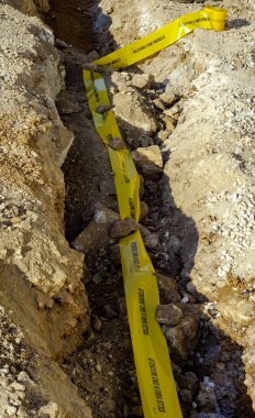 Fiber optik telekomünikasyon kablo dağıtım ağı üretmek için kıvrımlı plastik kablo kanallarını gömecek dar bir bölümle yapılan kazı.