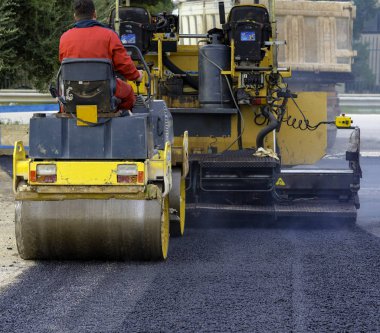 İşçi, asfaltı sıkıştırmak için titreşen yol silindirine önderlik ediyor.