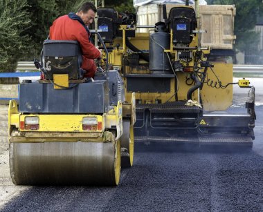 İşçi, asfaltı sıkıştırmak için titreşen yol silindirine önderlik ediyor.