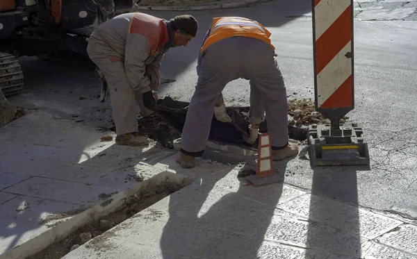 Execution of fiber optic distribution network for telecommunications. Workers position the cast iron manhole covers on manholes