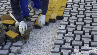 Paving taş işçisi bir şehir caddesinin inşaatı sırasında kaldırımları örülmemiş kumun üzerine yerleştiriyor ve yerine yerleştiriyor..