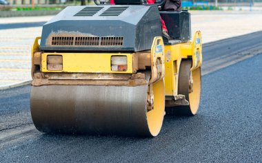 İşçi, asfaltı sıkıştırmak için titreşen yol silindirine önderlik ediyor.