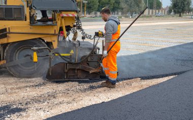 Worker regulate tracked paver laying asphalt heated to temperatures above 160 grades  pavement on a runway clipart