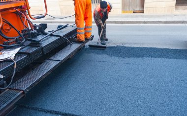 İşçi, bir pistte asfalt döşeyen ve 160 derecenin üzerindeki sıcaklıklara ısıtılan kaldırımları düzenler.