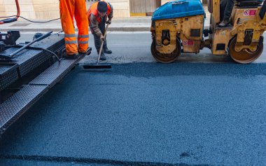 İşçi, bir pistte asfalt döşeyen ve 160 derecenin üzerindeki sıcaklıklara ısıtılan kaldırımları düzenler.