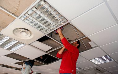 İnşaat işçisi asılmış tavanı alçıpanla birleştiriyor ve alçıpanı tornavidayla tavandaki metal çerçeveye yerleştiriyor..