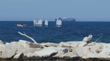 Bari, İtalya - 13 Haziran 2020: Bari rıhtımından yelkenli kullanmayı öğrenen çocuklarla birlikte küçük yelkenli tekneleri görebilirsiniz. Arka planda bir feribot görülebilir.