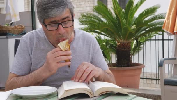 Senior Gentleman Sitting Terrace Eats Banana While Reading Book — Stock Video