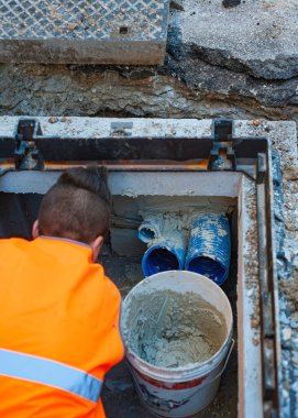 İnşaat işçisi veri iletim hattının bir çukurunu optik liflerle onarıyor, boruyu çimento havanıyla kapatıyor.