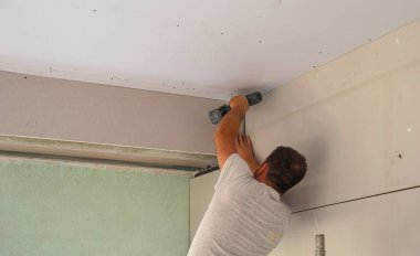 İnşaat işçisi asılmış tavanı bir alçıpanla monte ediyor. D, alçıpanı tornavidayla tavandaki metal çerçeveye yerleştiriyor.
