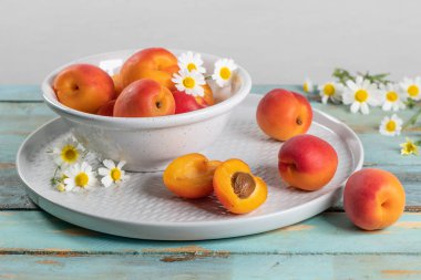 Tahta masadaki bir kasede lezzetli olgun kayısılar. Kayısılar ve papatya çiçekleriyle yakın plan.