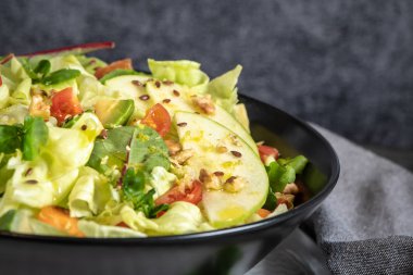 Salata. Bahar sebze salatası. Domatesli, elmalı, fındıklı, tohumlu ve limonlu taze sebze salatası. Salata kasesine zeytin yağı dökülüyor.
