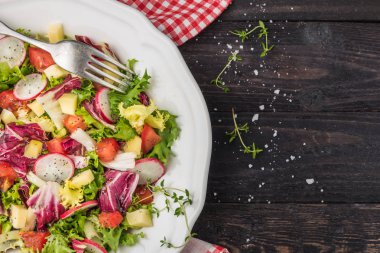 Karışık yeşillik, turp, peynir ve domates ahşap arka plan üzerine bir tabak içinde taze salata. İtalyan Akdeniz veya Yunan mutfağı. Vejetaryen vegan gıda. Üstten görünüm