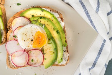 Avokado turp peynirli sandviç ve ahşap tahta üzerinde koyu arka plan üzerinde siyah ekmek üzerinde yumurta. Sağlıklı kahvaltı. Vejetaryen yiyecekler