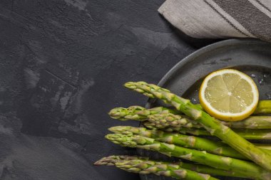 Bohça-in genç çiğ çiğ organik yeşil kuşkonmaz dilimlenmiş limon ve siyah doku arka plan üzerinde deniz tuzu. Üstten Görünüm. Sağlıklı beslenme