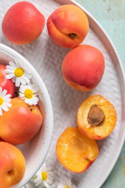 Tahta masadaki bir kasede lezzetli olgun kayısılar. Kayısılar ve papatya çiçekleriyle yakın plan.