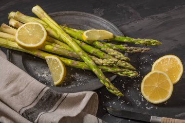 Bohça-in genç çiğ çiğ organik yeşil kuşkonmaz dilimlenmiş limon ve siyah doku arka plan üzerinde deniz tuzu. Üstten Görünüm. Sağlıklı beslenme