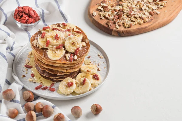 Pancakes with banana, walnuts, goji and honey. Healthy breakfast. On white wooden table background. Top view