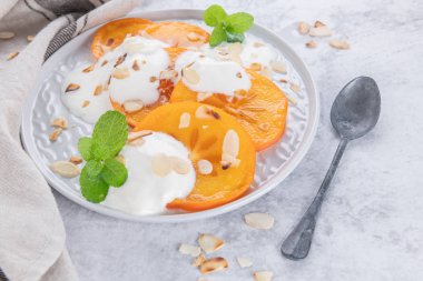 Yoğurt ve badem ile dilimlenmiş Trabzon hurması. Açık renkli sağlıklı gıda konsepti