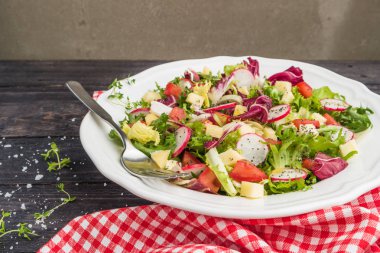 Karışık yeşillik, turp, peynir ve domates ahşap arka plan üzerine bir tabak içinde taze salata. İtalyan Akdeniz veya Yunan mutfağı. Vejetaryen vegan gıda. Üstten görünüm