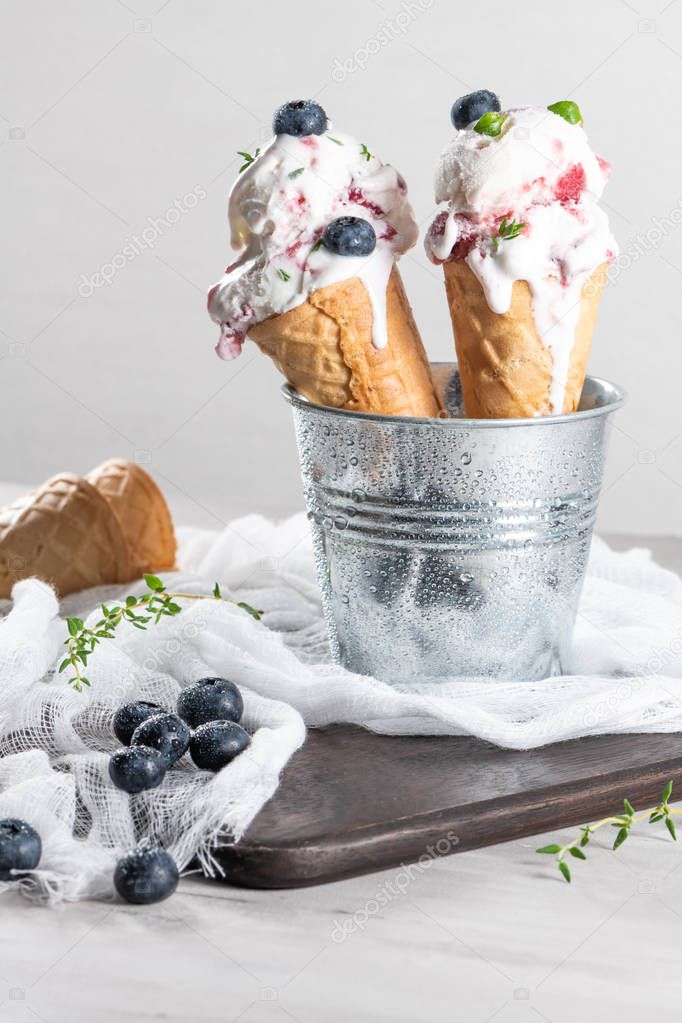 Homemade blueberries ice cream in waffle cones with fresh blueberries and thyme leaves