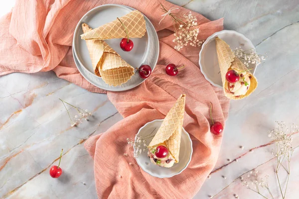 Coni di cialde tradizionali con gelato e frutti di ciliegia sulla superficie in pietra di marmo — Foto Stock